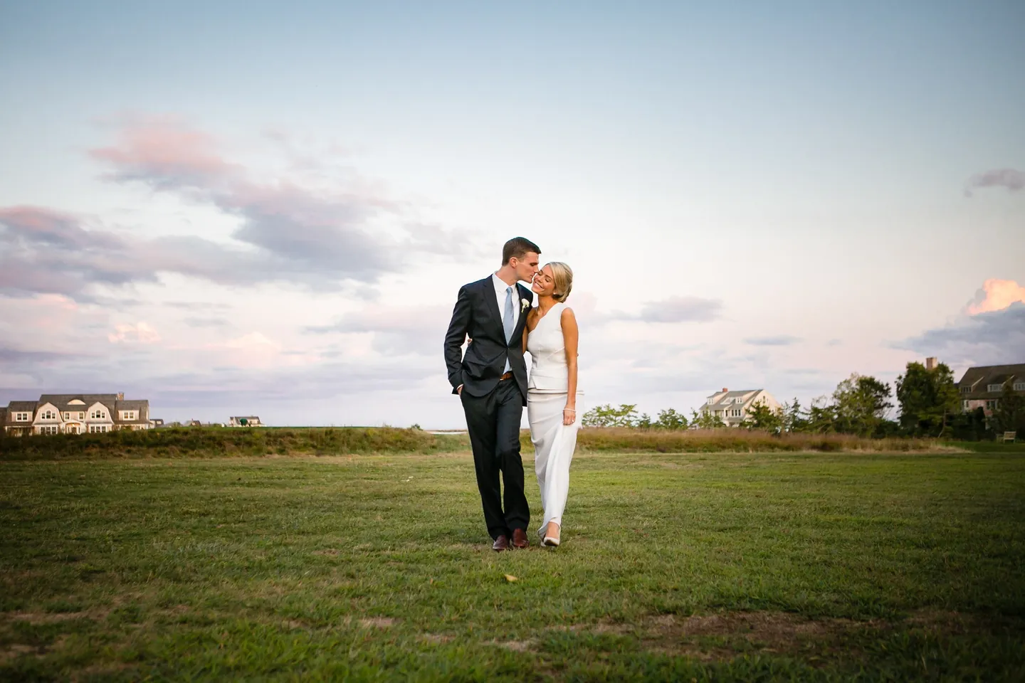 Kristen and Charlie kiss in an open field under a pastel pink sunset sky