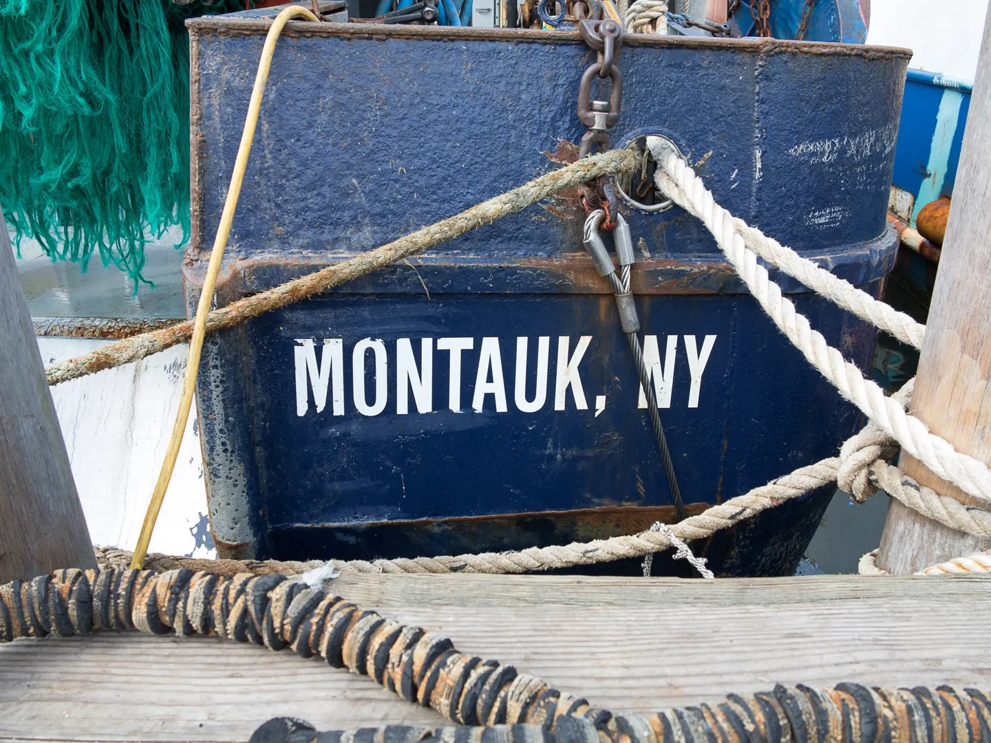 A blue fishing boat stenciled Montauk, NY, with thick ropes coiled on the dock beside it