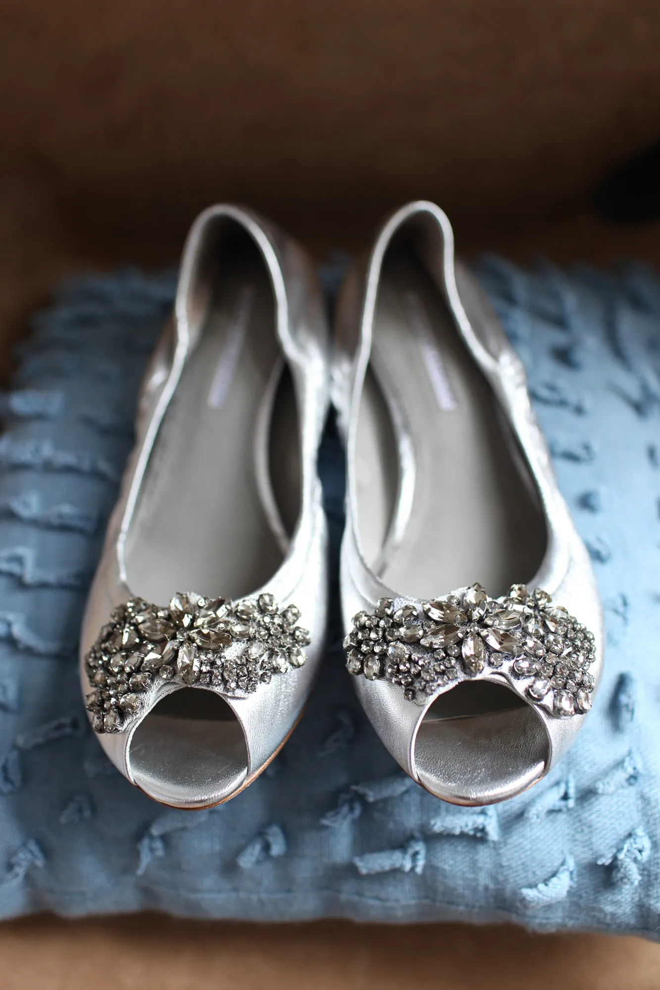 Silver jeweled peep-toe flats resting on a pale blue cushion