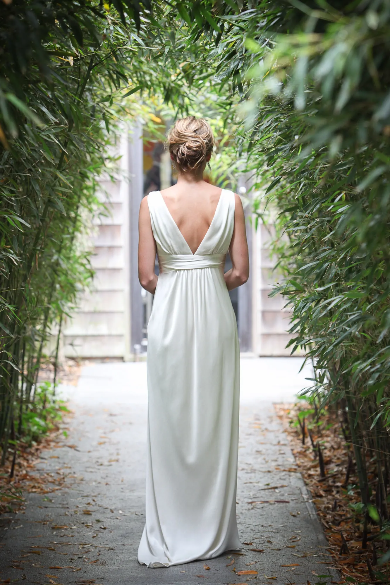 The bride walks away down a narrow path walled in tall green bamboo