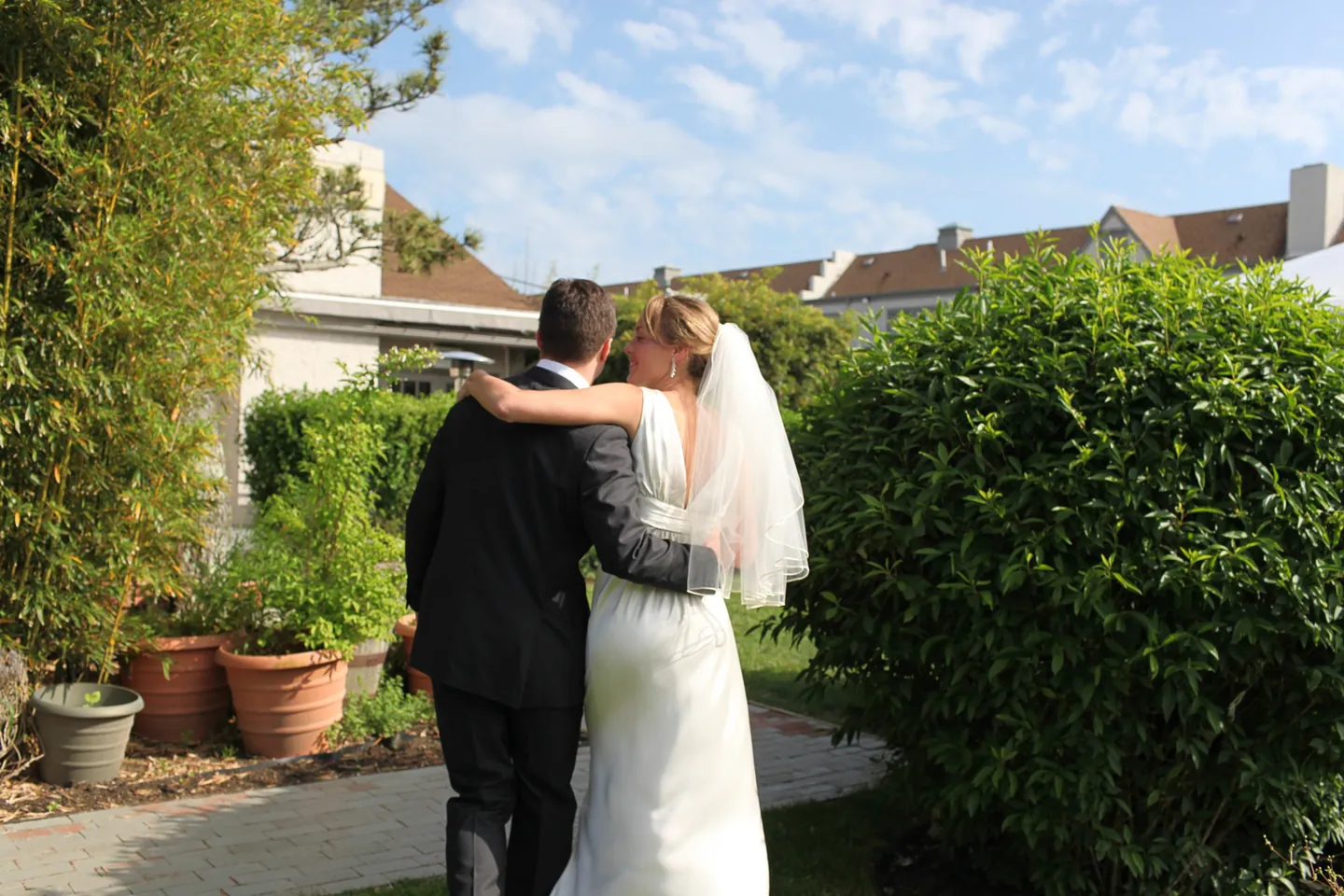 Kyla and Caley kiss beside a hedge and potted plants in the late sun