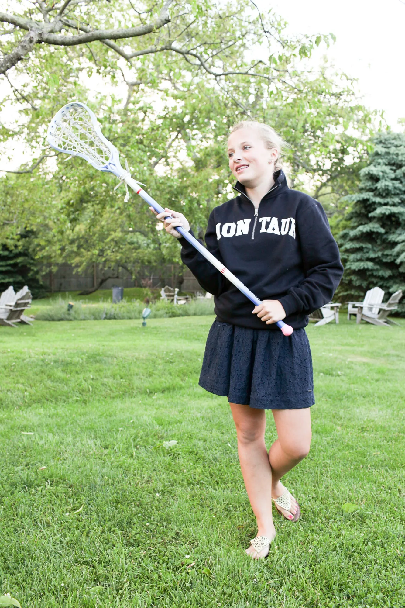 A young guest in a Montauk sweatshirt carries a lacrosse stick across the lawn
