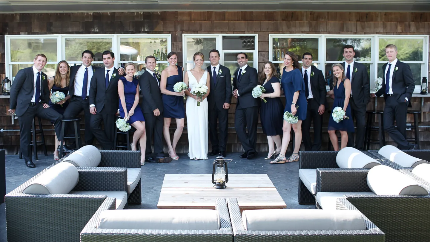 The full wedding party lines up on a stone patio with lounge furniture in front