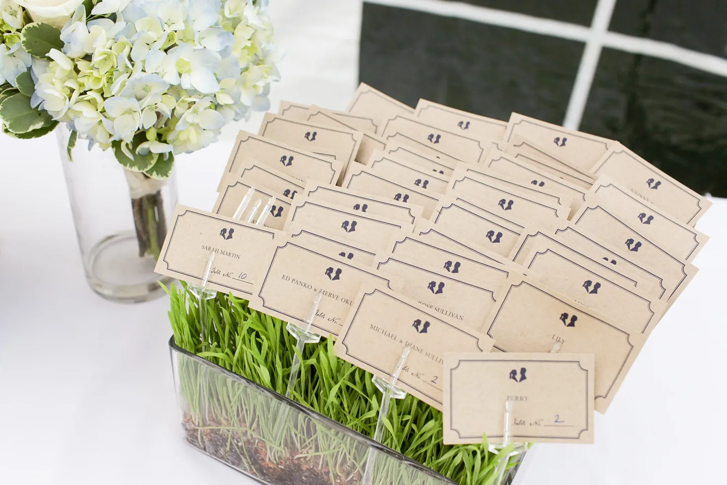 Rows of cream escort cards tucked into trays of fresh wheatgrass beside white flowers
