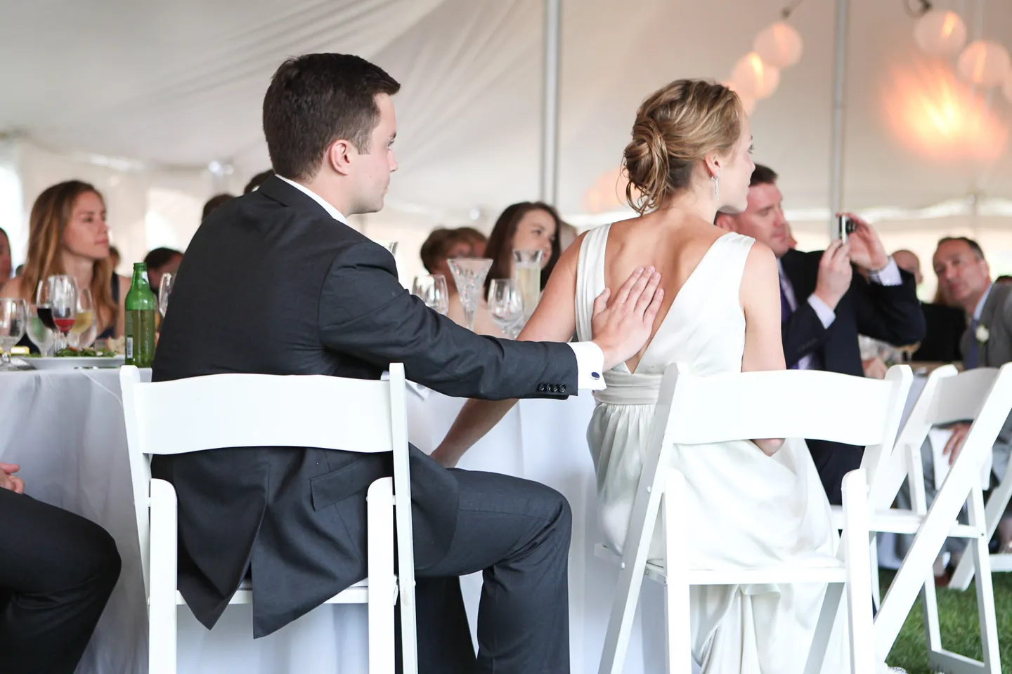The couple sit together at a tent table among guests during dinner