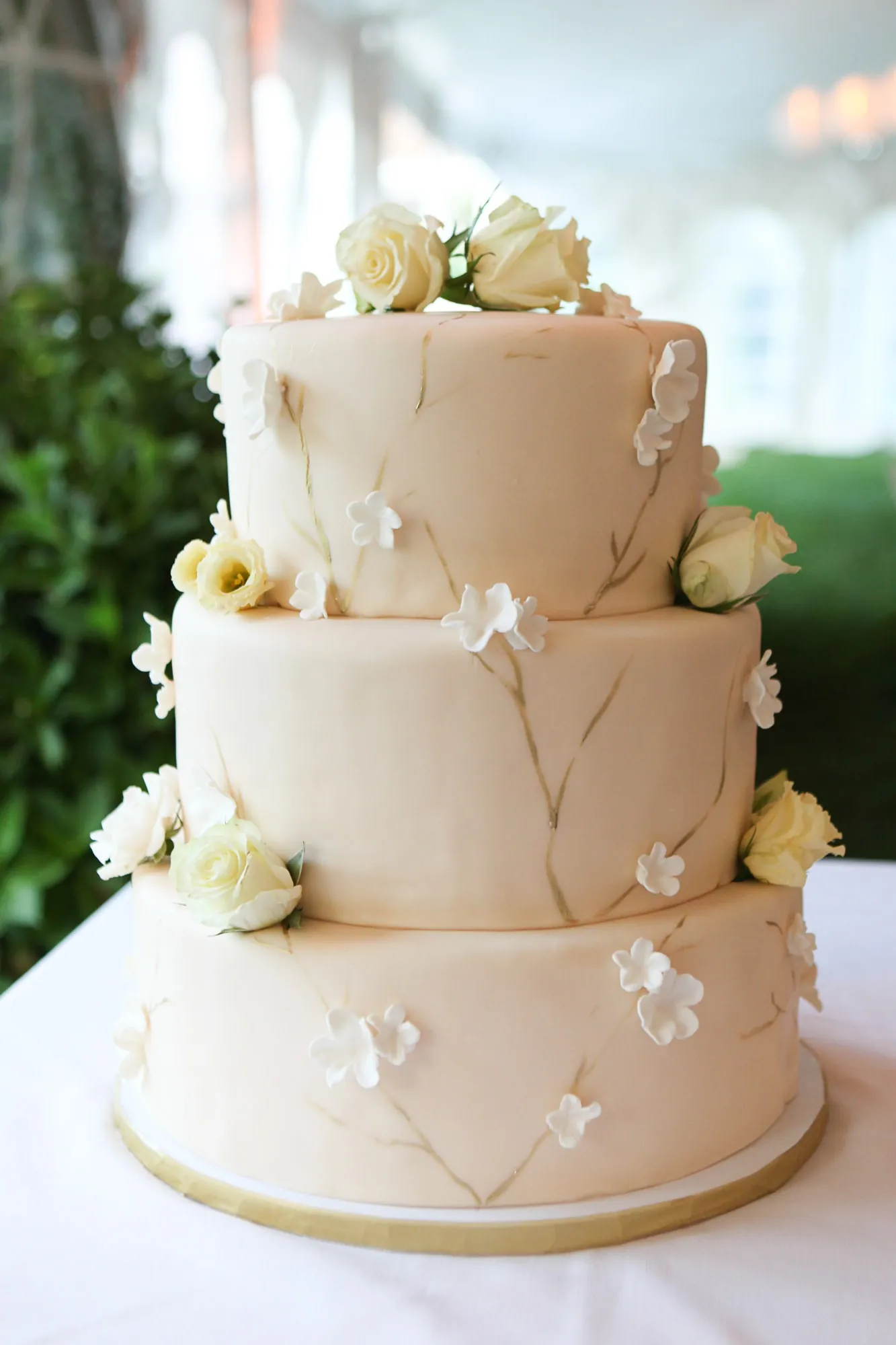 A tiered cream wedding cake decorated with sugar flowers and piped detail