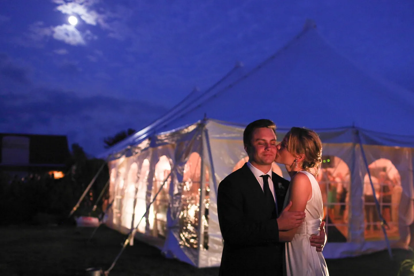 Kyla and Caley share a cheek kiss outside the glowing tent as the moon rises