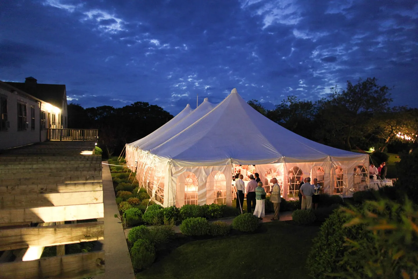 The white pole tent glows at dusk beyond garden steps and low path lights