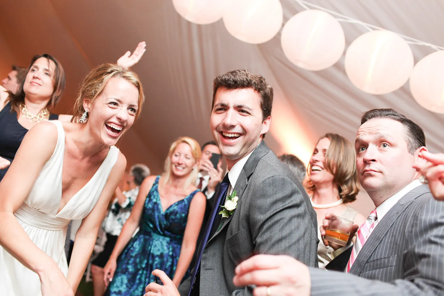 The bride laughs and dances with guests beneath white paper lanterns