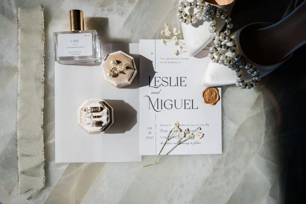 Leslie and Miguel's invitation with a gold wax seal, ring boxes, and perfume on marble