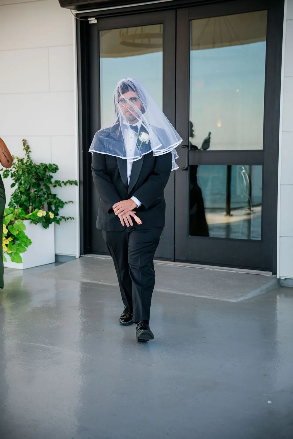 Best man walks through a doorway wearing a long wig and a bridal veil