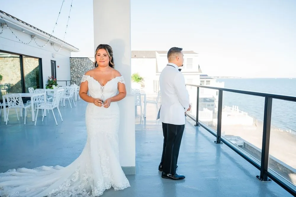 Leslie and Miguel stand on either side of a white column on the balcony for their first touch