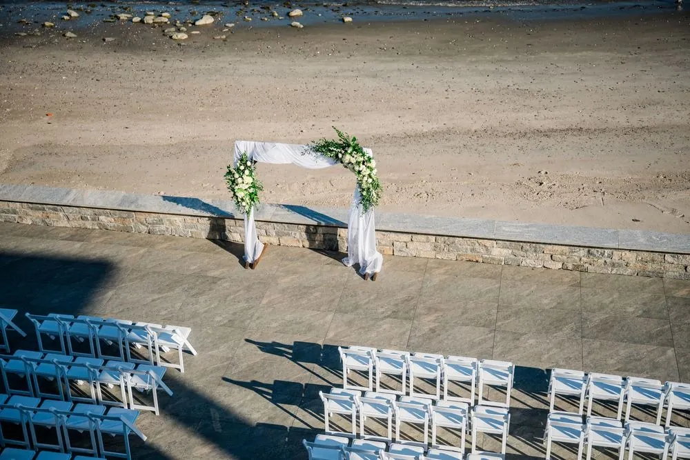 Aerial view of the terrace ceremony setup, white arch and chairs above the beach
