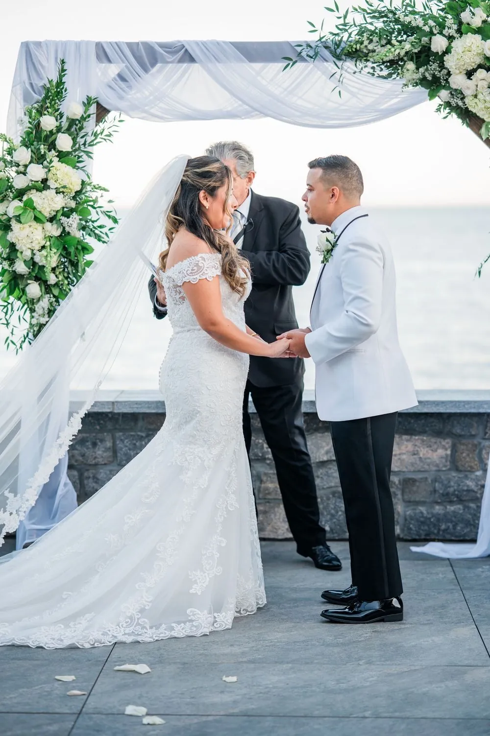 Leslie and Miguel hold hands under the rose and greenery arch as the officiant speaks