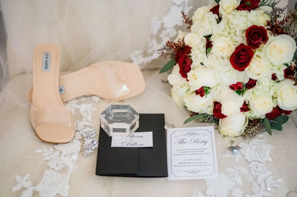Clear heels, a red and white rose bouquet, invitation suite and an acrylic ring box on lace