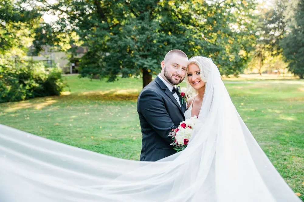 Lexy and Dillon smile cheek to cheek as her long veil sweeps across the grass
