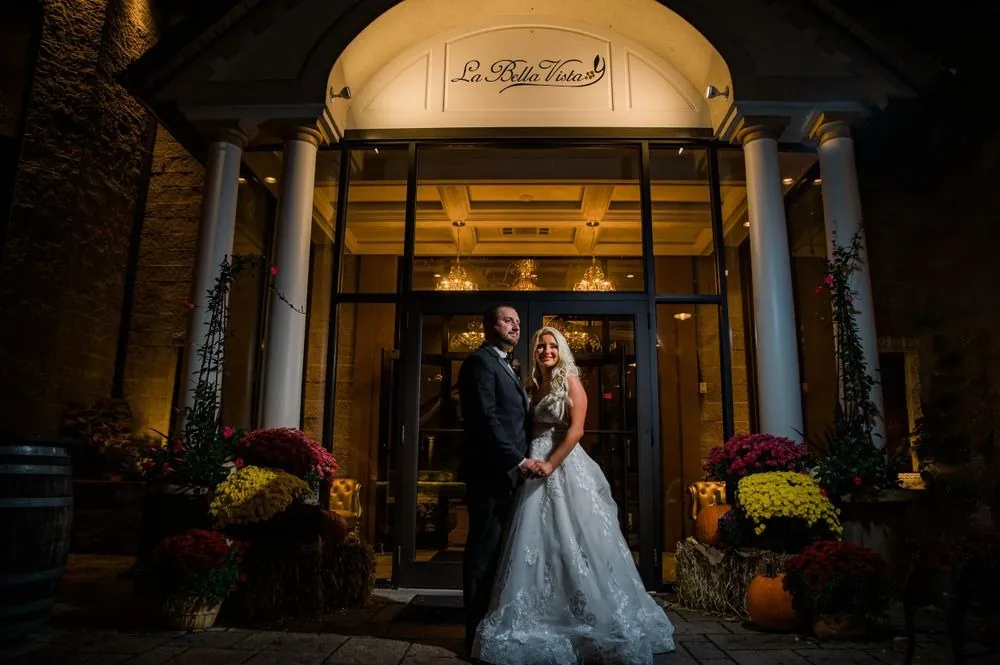Lexy and Dillon stand at the lit entrance of La Bella Vista between mums and pumpkins