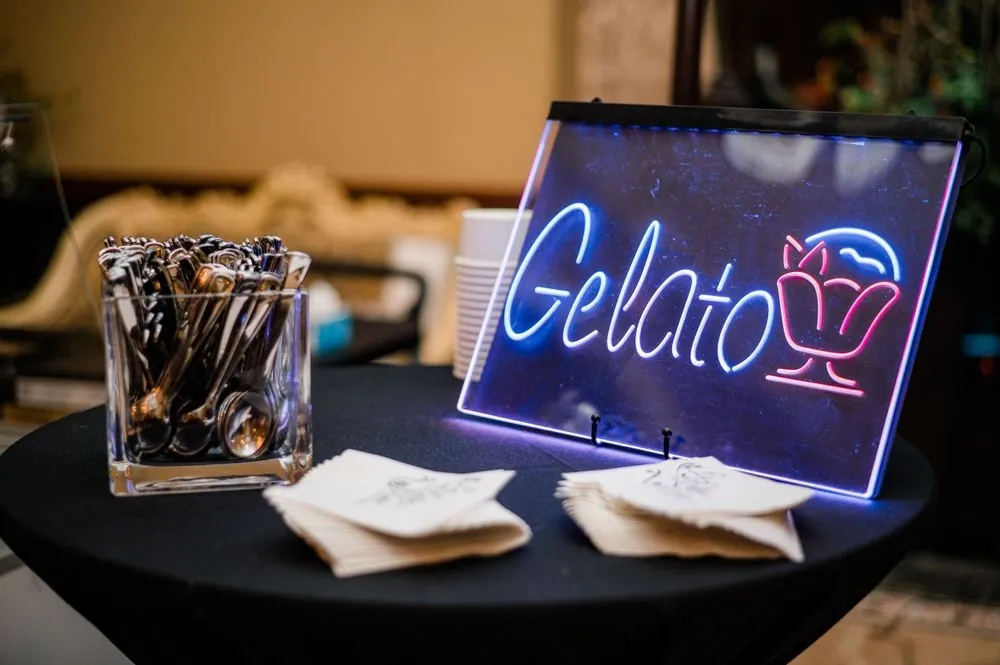 A glowing gelato sign and napkins set out on a dark table at the reception