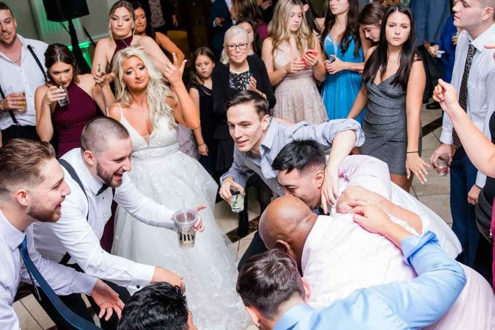 Friends crowd around the bride on the dance floor, cups raised high