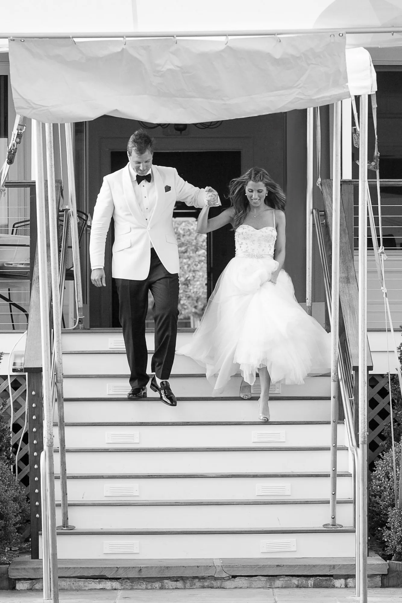 Black and white frame of Maddie and Dave stepping down a canopied stair, her skirt gathered in hand