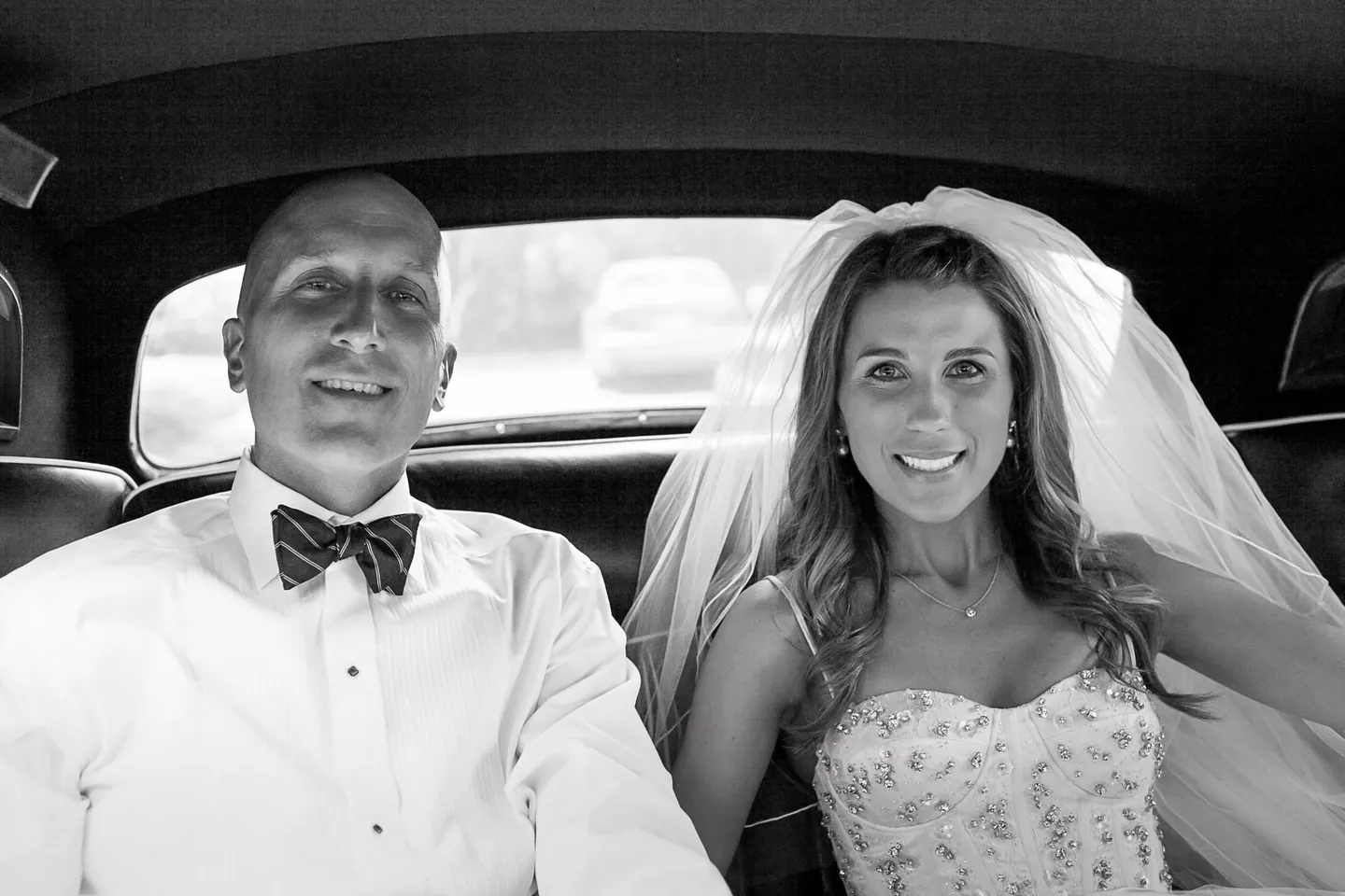 Black and white frame of Maddie and Dave smiling in the back seat of a vintage car