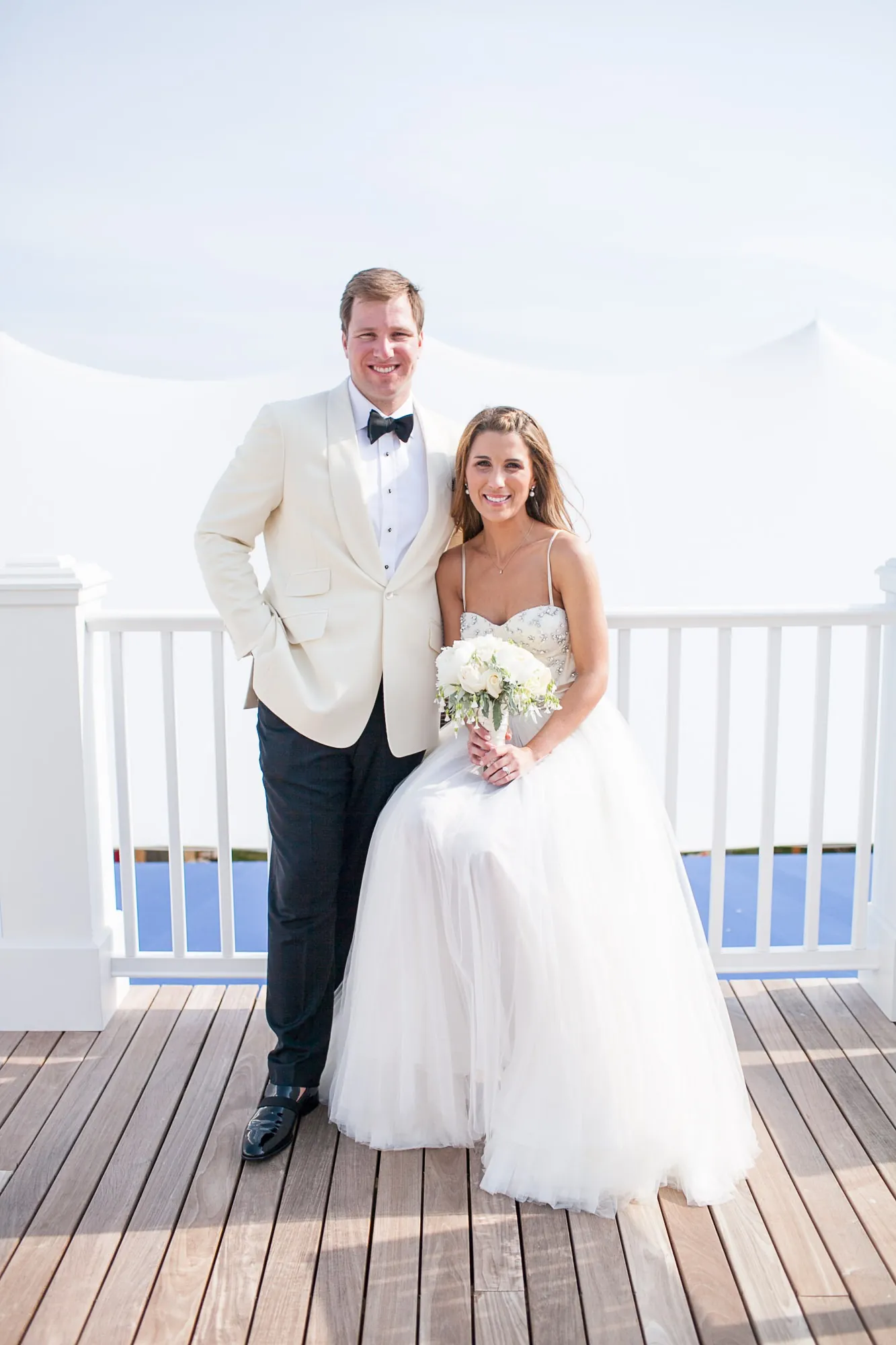 Maddie and Dave stand on a white dock with the harbor behind them