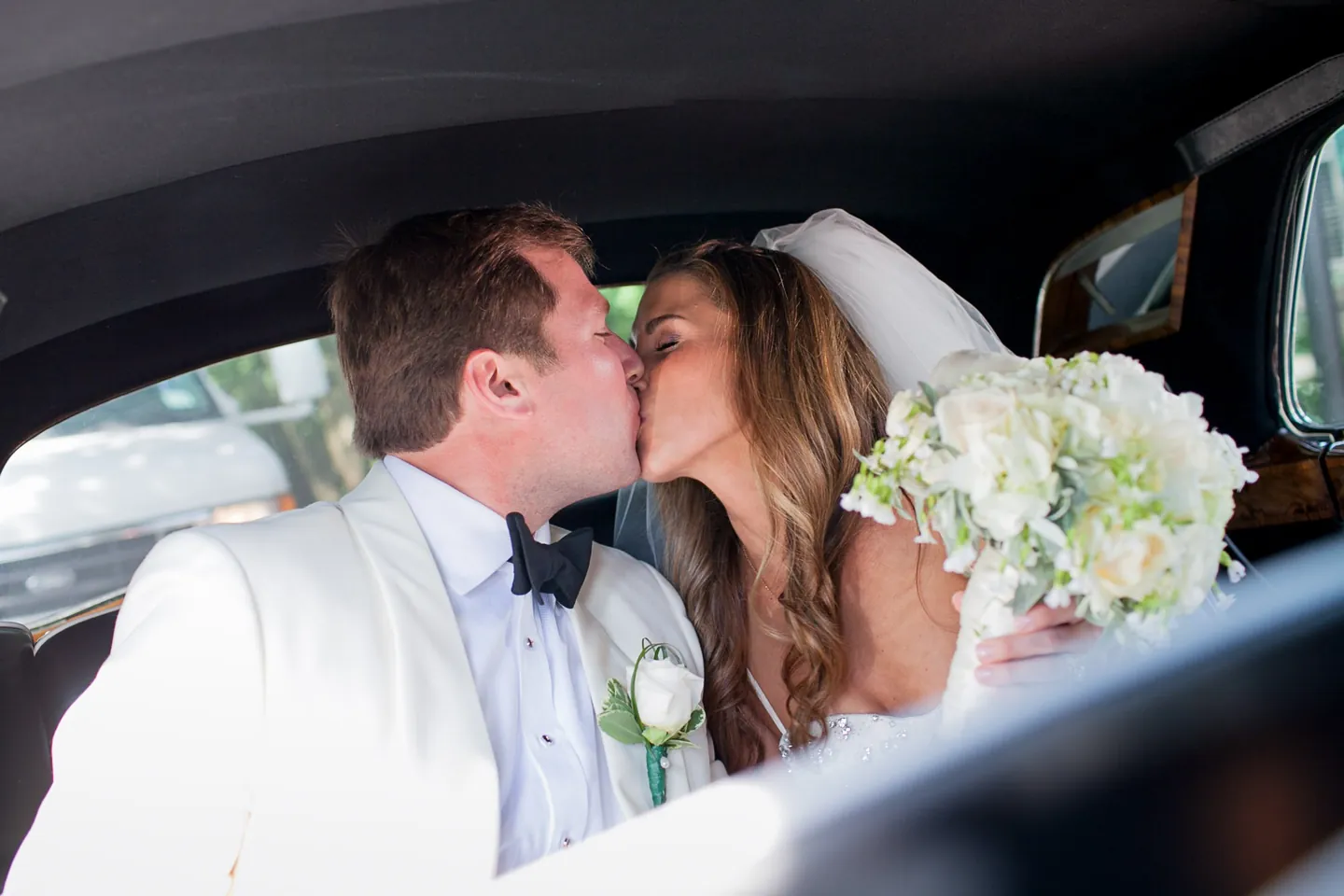 Maddie and Dave kiss in the back of the vintage car, her hydrangea bouquet between them