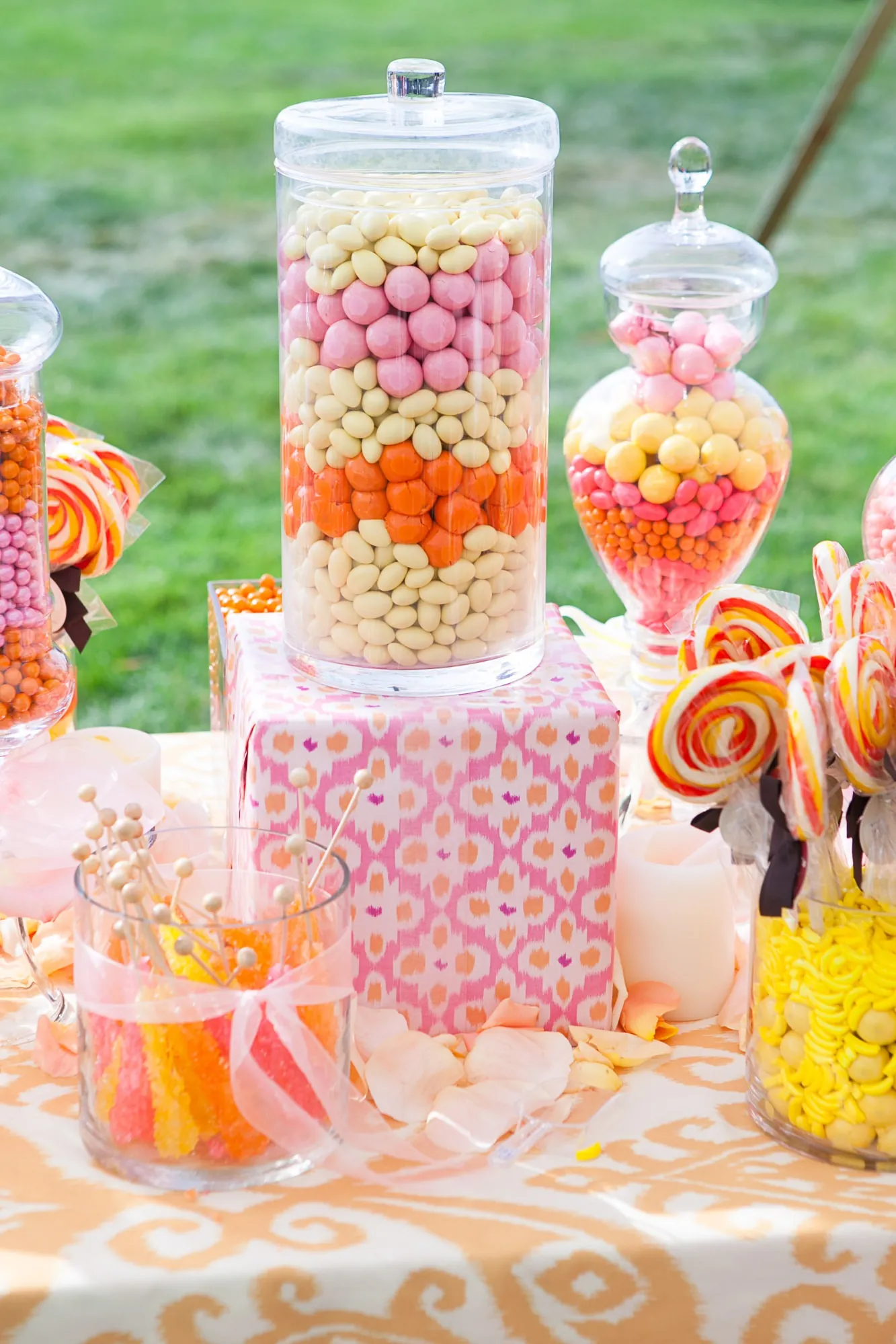Glass jars of pastel candy and swirl lollipops on a patterned table on the lawn
