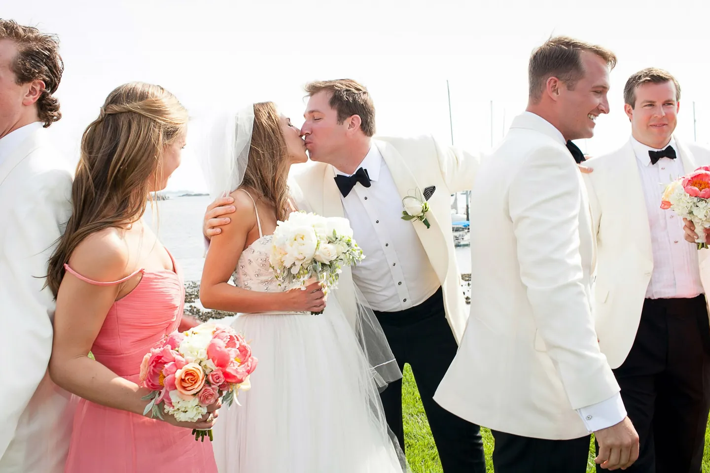 Maddie and Dave kiss as bridesmaids and groomsmen in white jackets stand around them