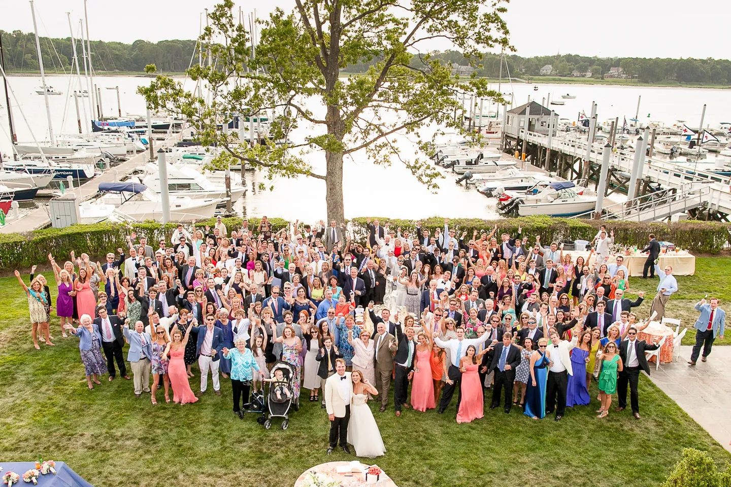 Overhead view of guests waving on the club lawn with the marina and moored sailboats behind