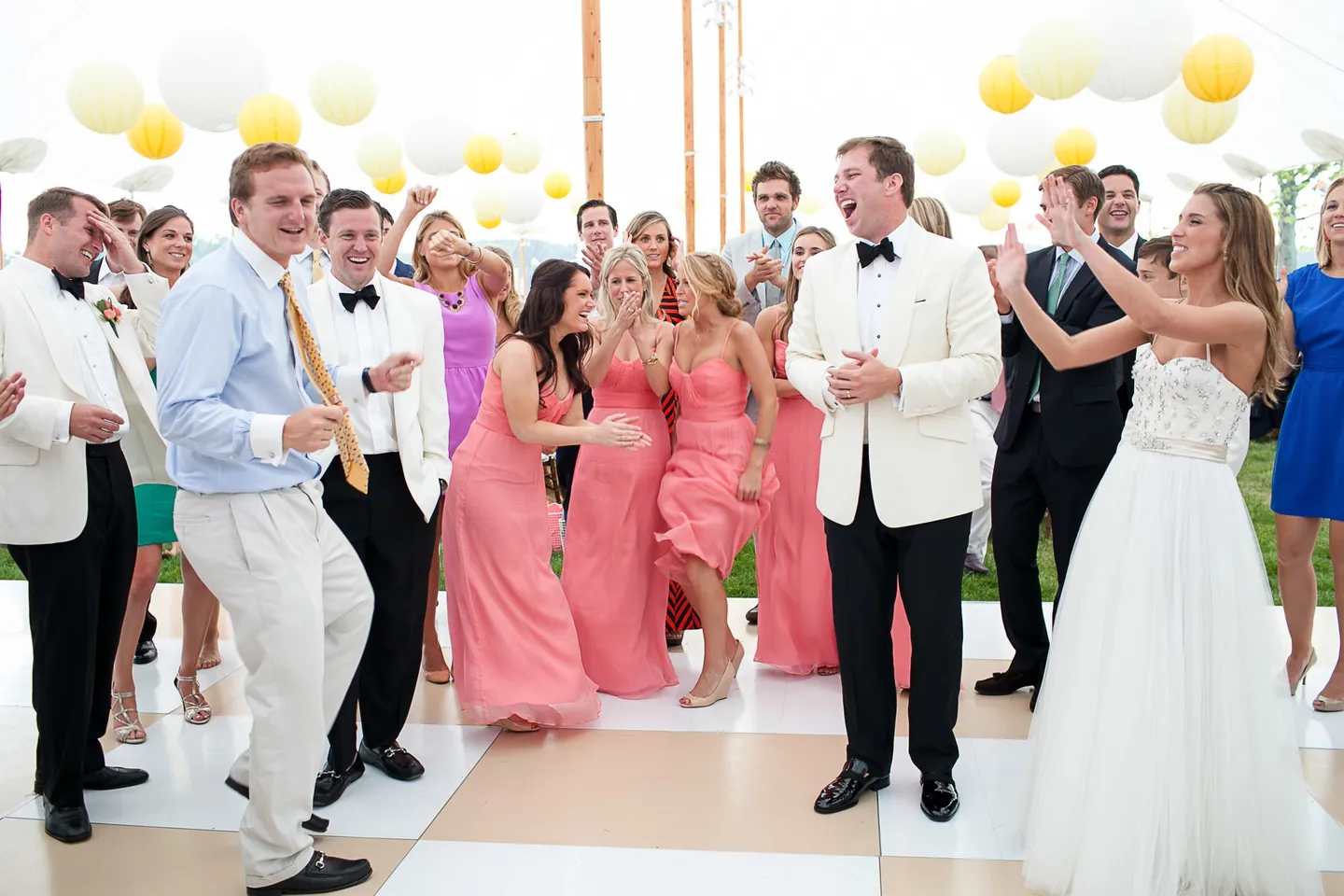 The wedding party dances under yellow and white paper lanterns in the tent