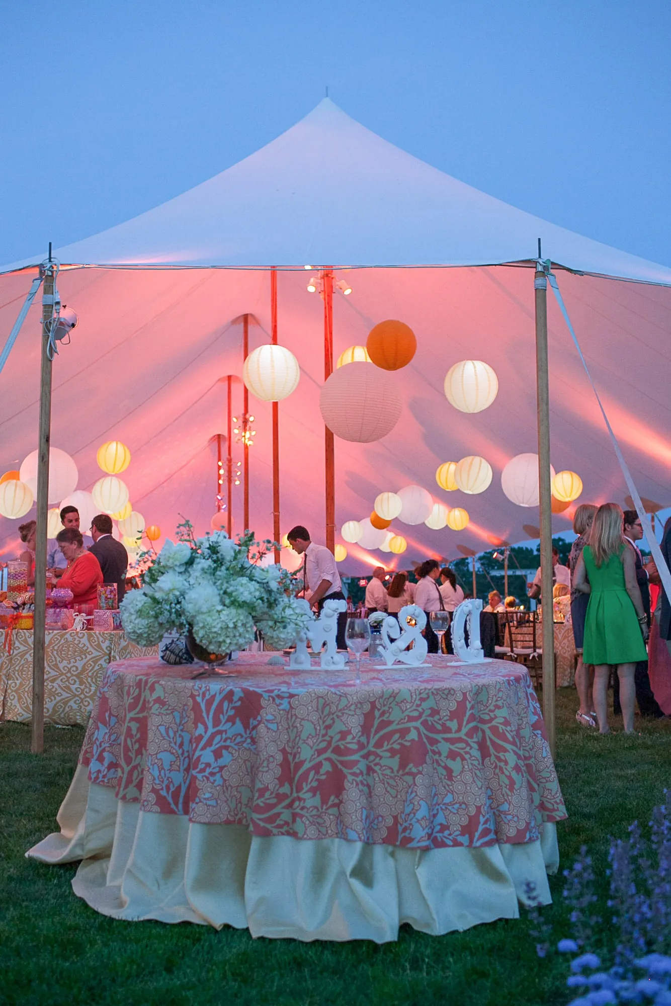 A round table in pink linens under lanterns as the tent glows at dusk