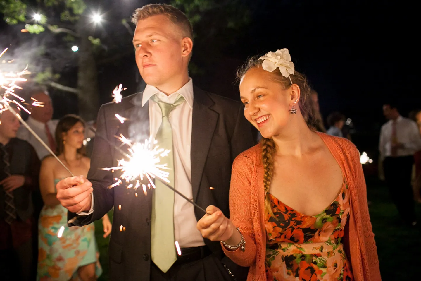 Guests light sparklers in the dark, faces glowing in the sparks