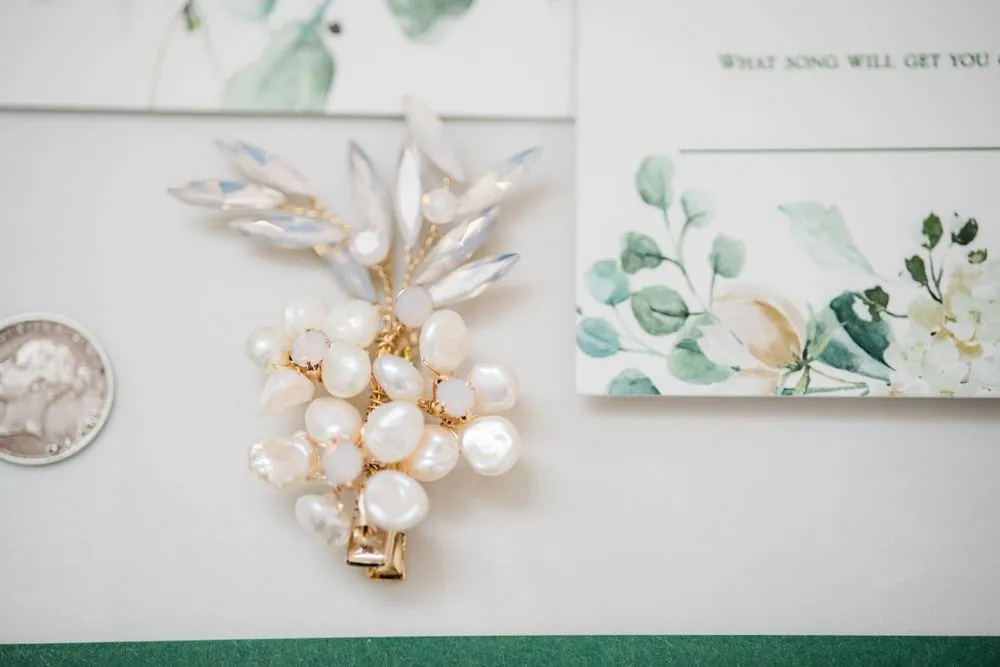 A pearl bridal hair comb resting beside a white invitation with green leaves