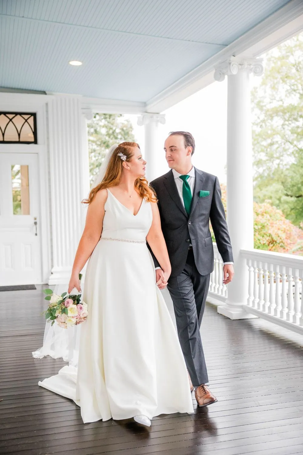 Maggie and Andrew walk hand in hand along the long covered porch