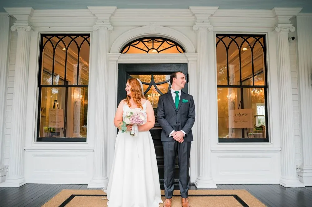 The couple stands at the arched front door of the house