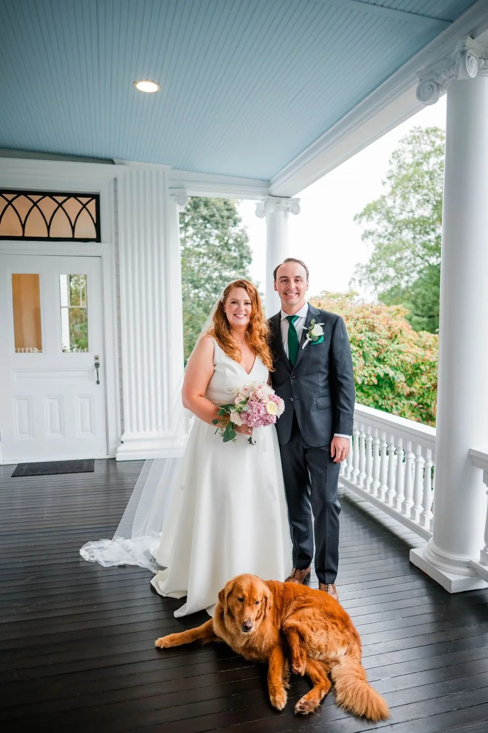 Maggie and Andrew smile on the porch as a golden retriever lies at their feet