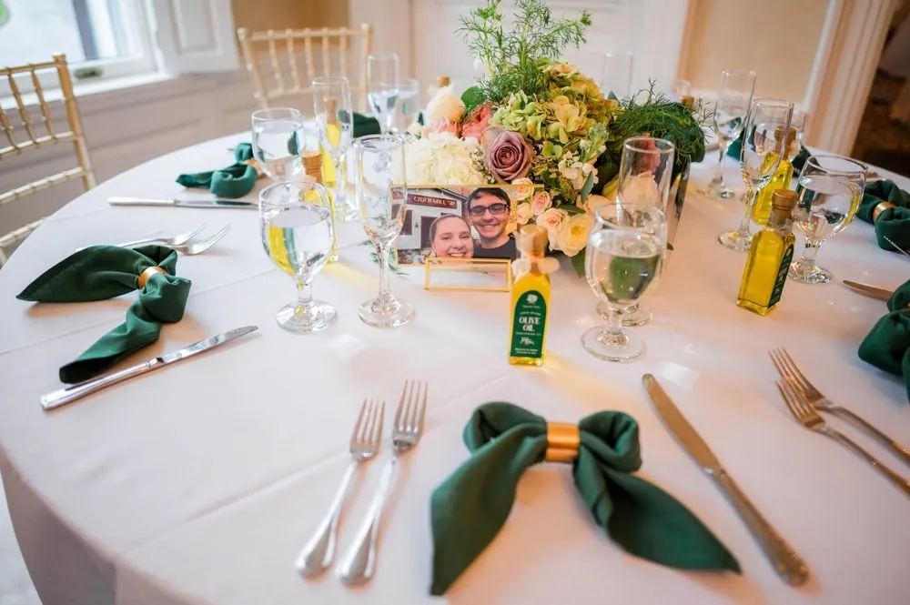A round reception table with green napkins, gold flatware and small bottle favors