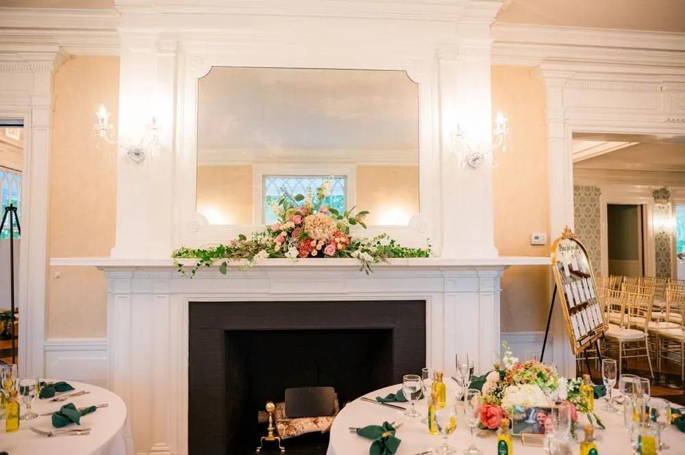 A reception room set around a white fireplace with low floral centerpieces