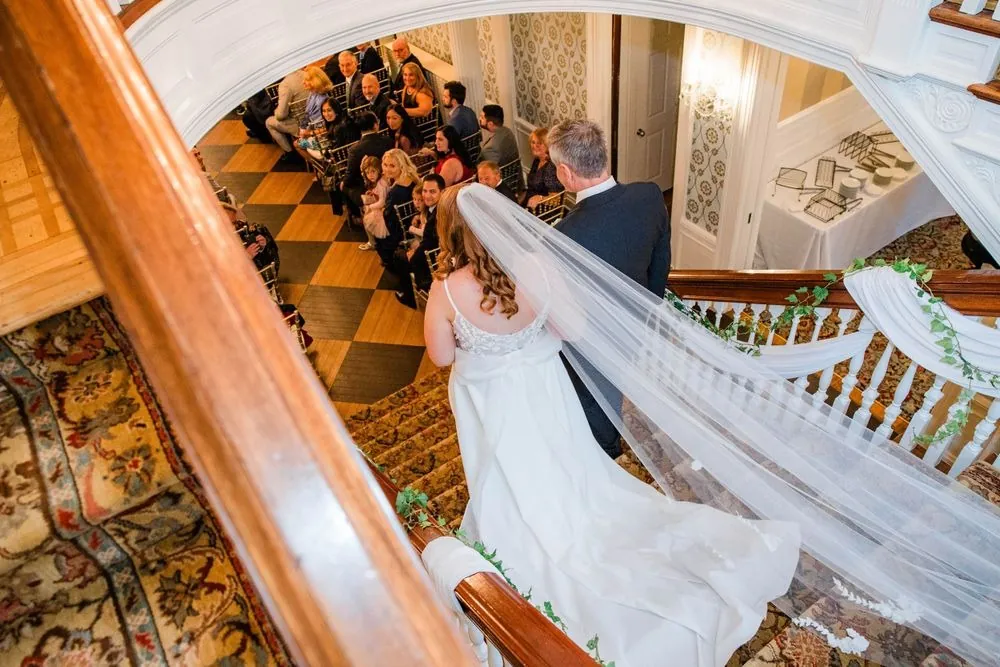 The bride descends the curved staircase as her long veil spills over the banister