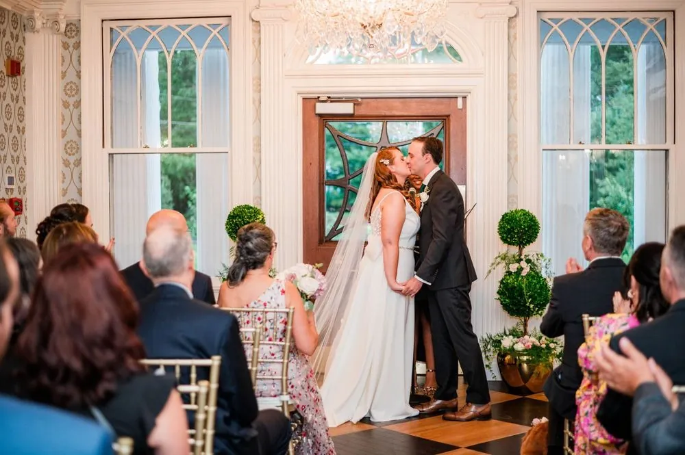The newlyweds kiss as guests applaud from both sides of the parlor