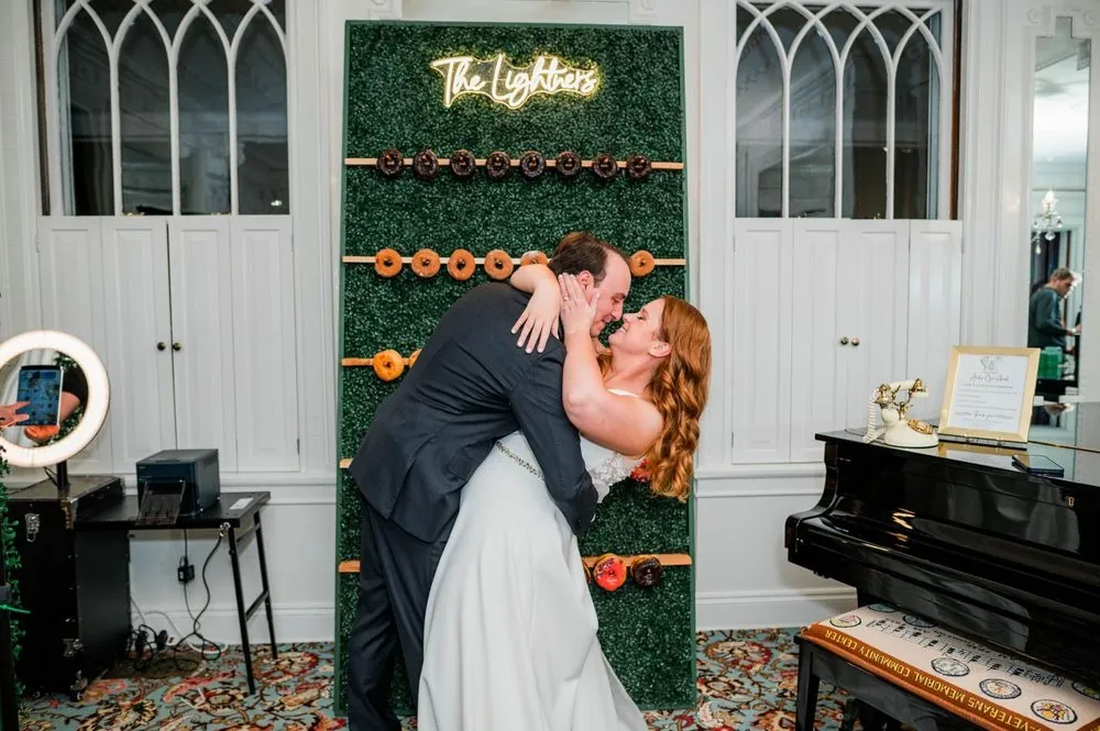 The groom dips the bride for a kiss in front of a donut wall