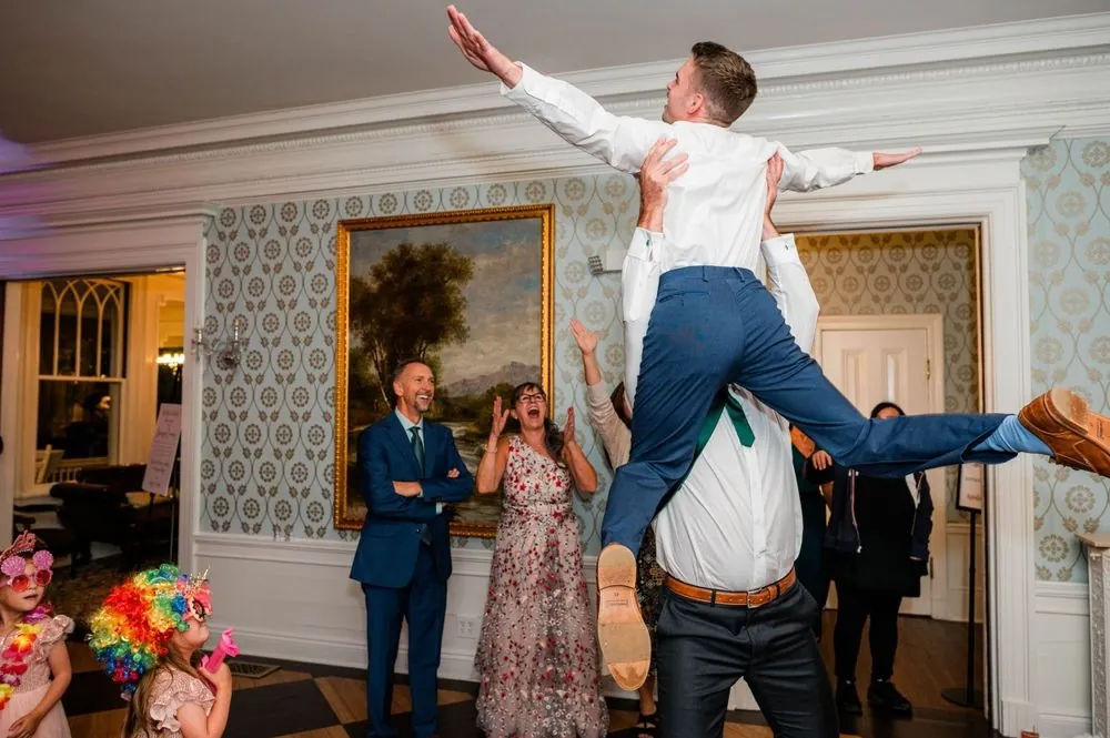 A groomsman leaps high over the dance floor as guests watch