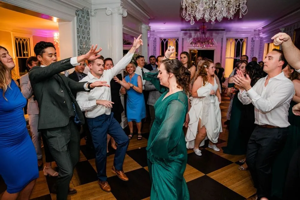 Guests dance with arms up under purple light in the crowded parlor