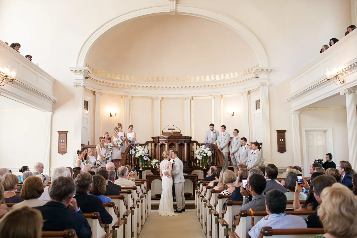 Wide view of the white church interior with the couple at the altar and full pews