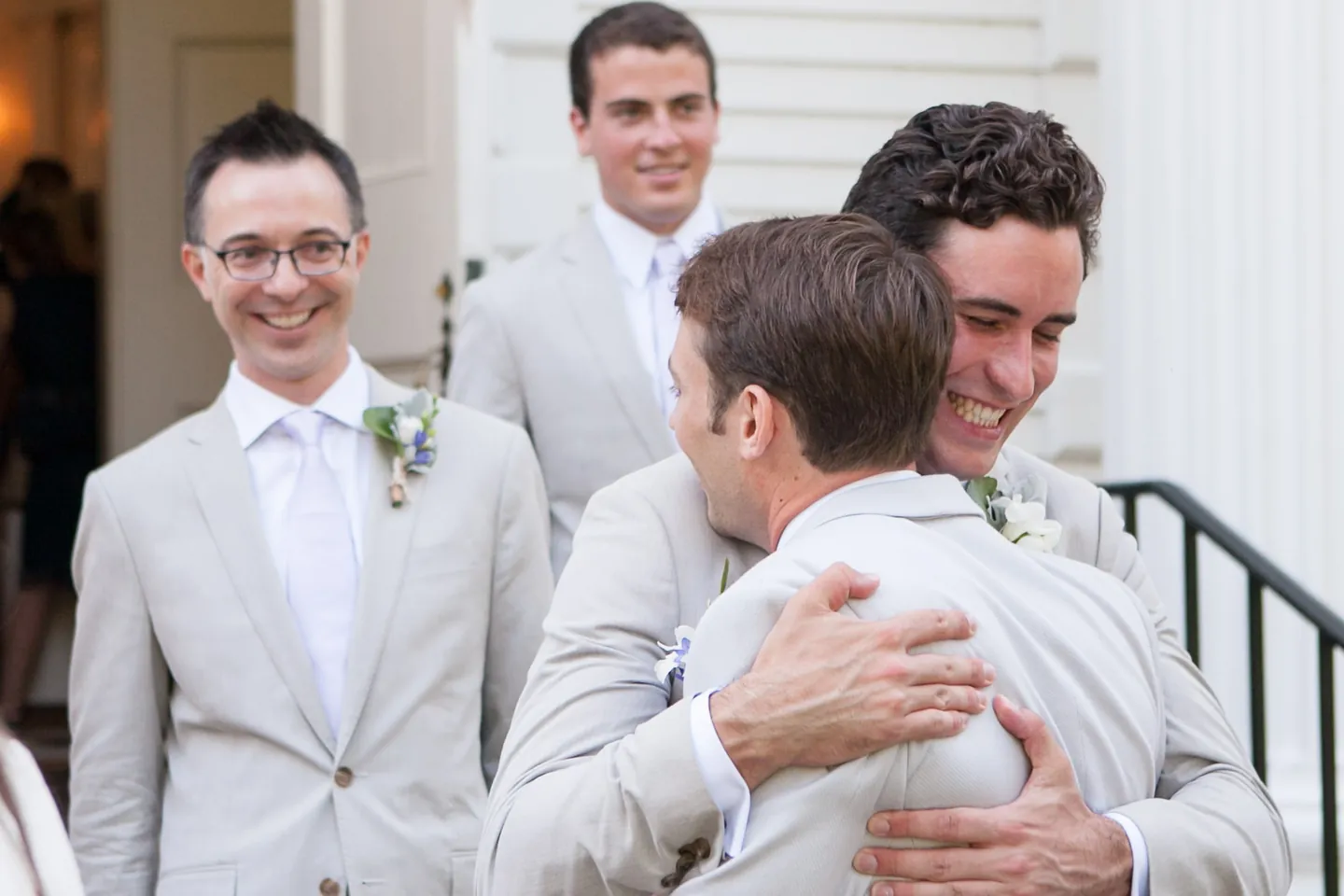 Groomsmen in light grey suits hug and laugh on the church steps