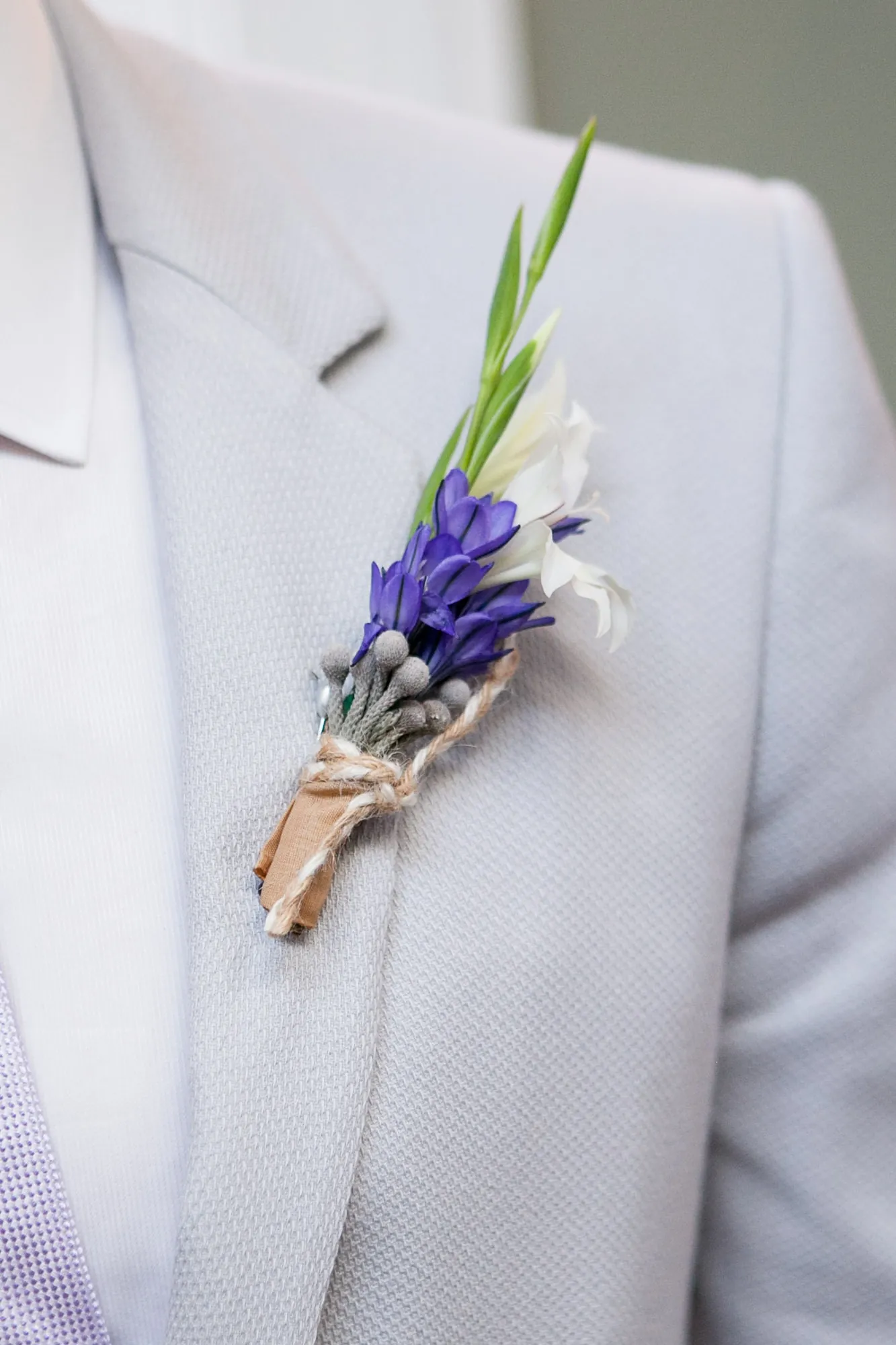 A lavender and greenery boutonniere pinned to a pale grey lapel