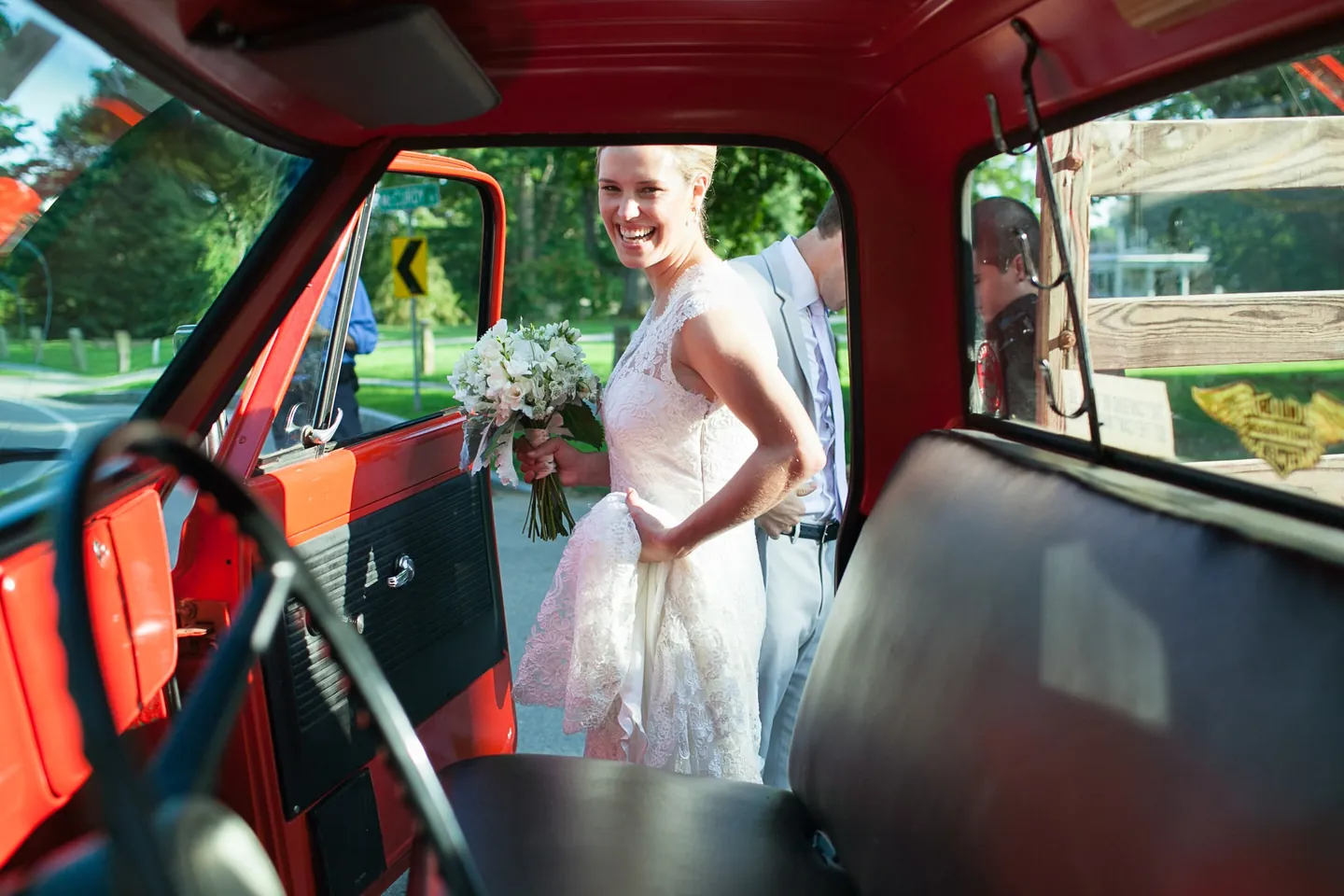 The bride climbs into the cab of a red vintage pickup in her lace gown