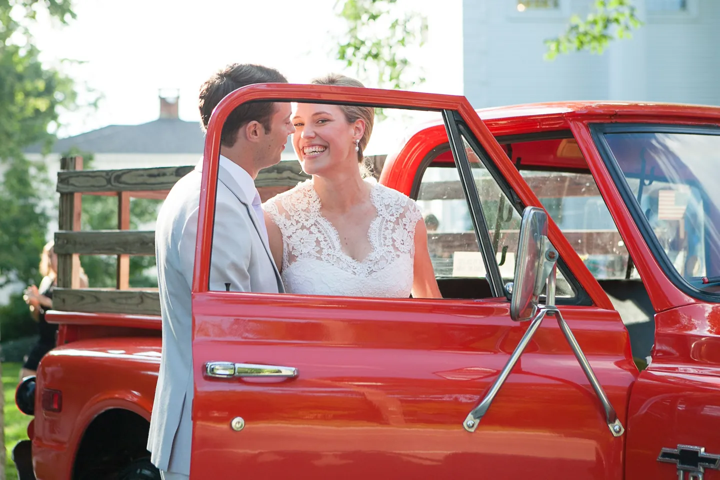 Marina and James stand at the open door of the red pickup, both smiling