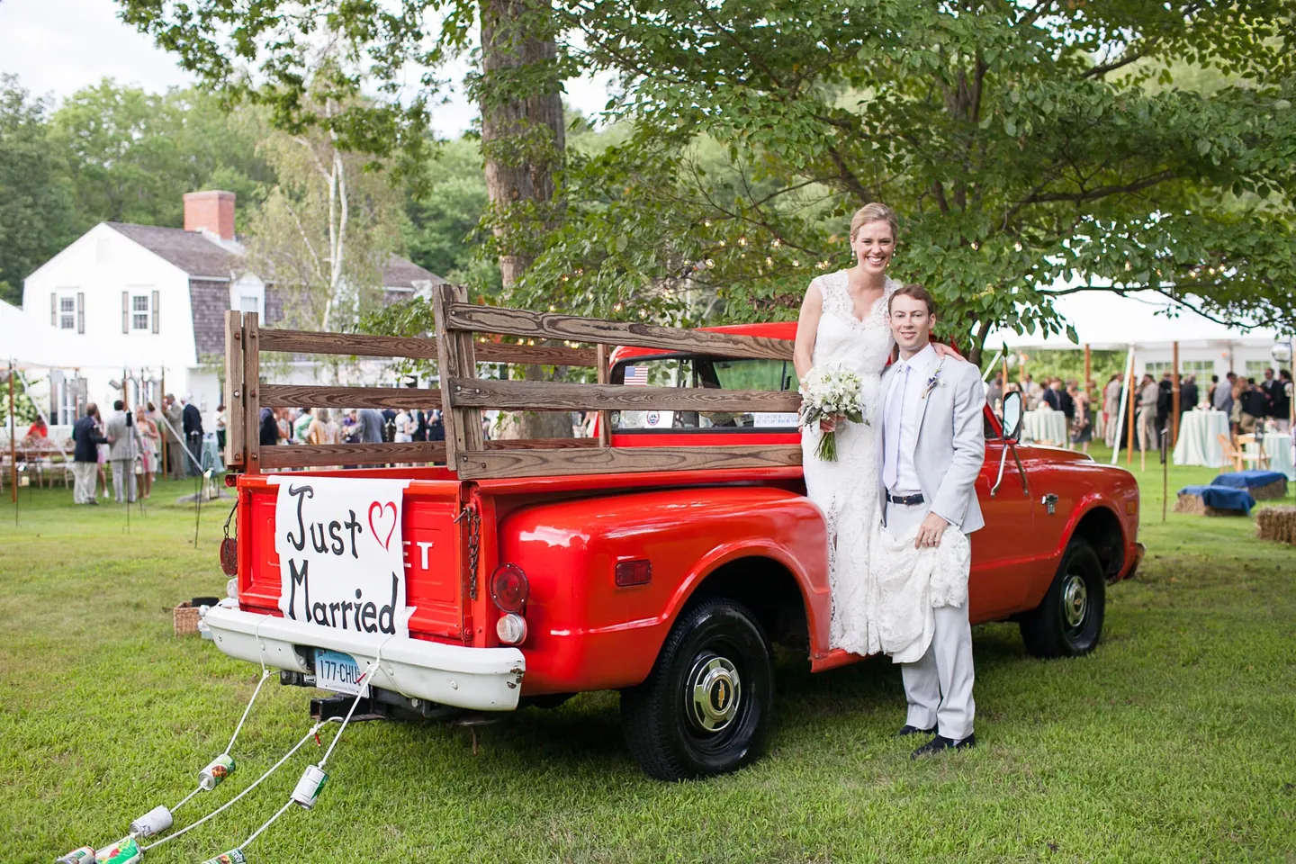 Marina and James stand in the bed of a red pickup with a Just Married sign on the tailgate